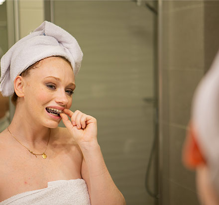 Kobieta w łazience zdejmująca ortodontyczną przezroczystą nakładkę prostującą 1