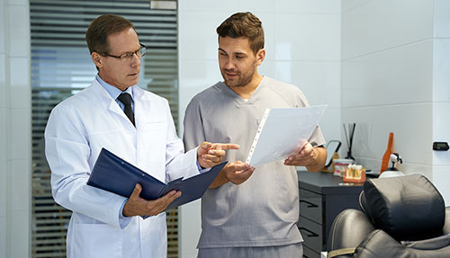 Gabinet ortodontyczny dwóch mężczyzn w kitlach medycznych trzymają w rękach skoroszyt i kartkę 1