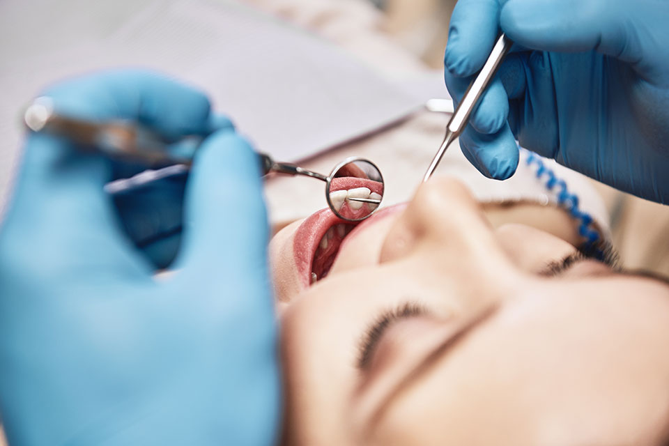 Pacjent poddawany przeglądowi stomatologicznemu, otwarte usta, ręce w rękawiczkach, lusterko 1