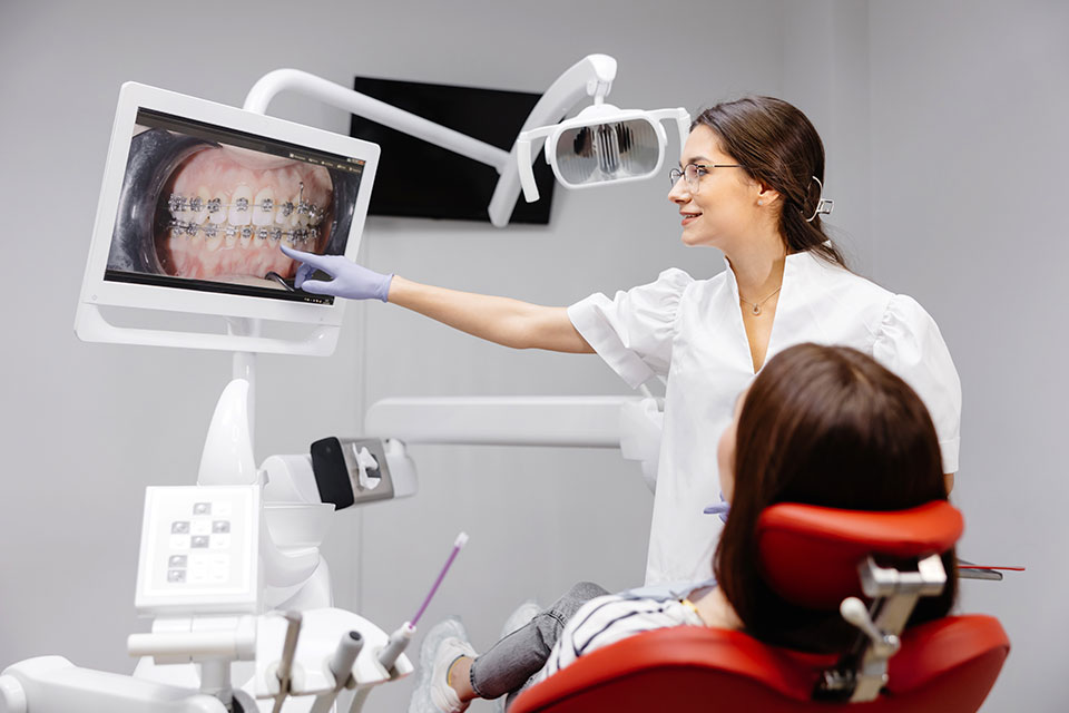 Gabinet, fotel stomatologiczny, pacjent i osoba w kitlu medycznym, na monitorze widoczne łuki zębowe z aparatem ortodontycznym 1